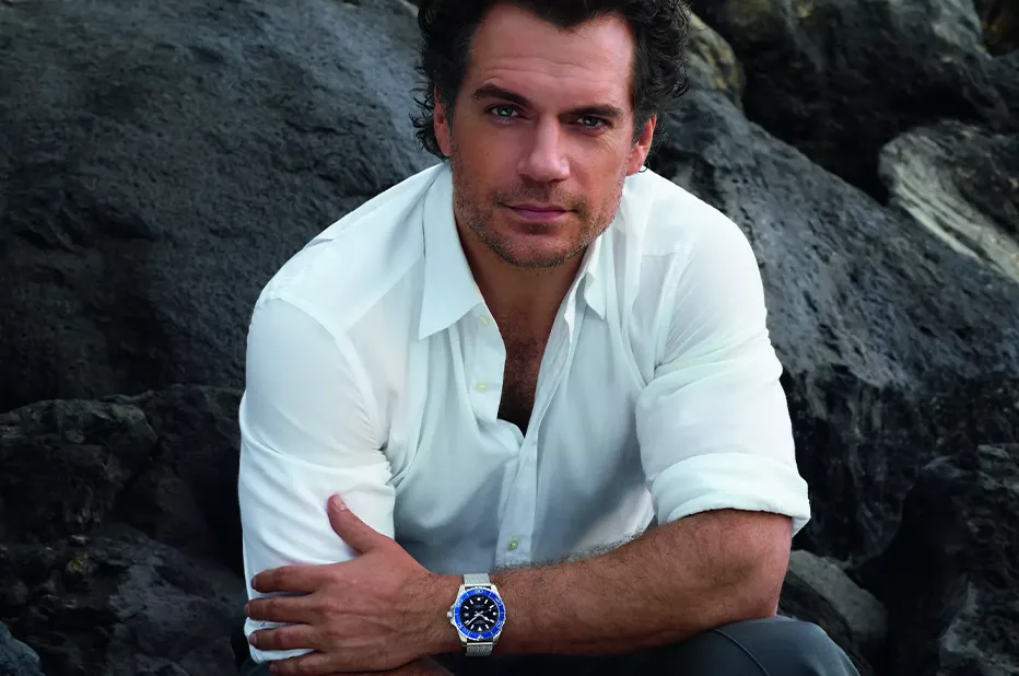 Henry Cavill na skalnatém pobřeží s hodinkami Longines HydroConquest s modrou keramickou lunetou na zápěstí